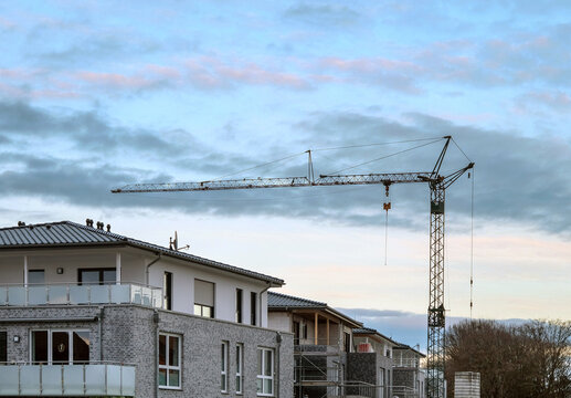 Konzept Baustelle Siedlung: Blick auf einen großen Baukran in einem Neubaugebiet mit fertigen HÃ¤usern und Baustellen im Abendlicht
