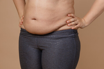 Naklejka premium Front view of overweighted thick belly of woman wearing leggings. Body positive. Violation of cell elasticity, loss of nutrients. Sagging skin after pregnancy or sudden weight loss.