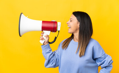 Caucasian girl isolated on yellow background shouting through a megaphone to announce something in lateral position