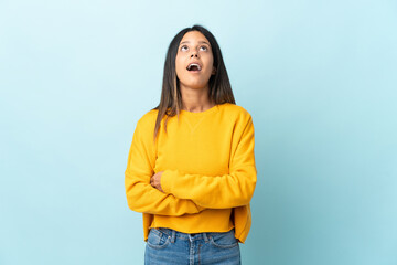 Caucasian girl isolated on blue background looking up and with surprised expression