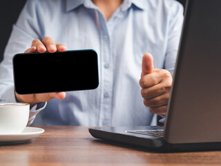 Hand holding a horizontal mobile phone with a blank black screen and show thumbs up while sitting in the office