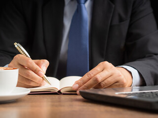 Close-up of a businessman holding a pen writing on paper on a desk while sitting in the office