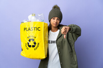 Young woman holding a bag full of plastic showing thumb down with negative expression