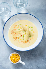 Plate of corn soup with addition of baby corncobs, vertical shot on a light-blue stone background, selective focus
