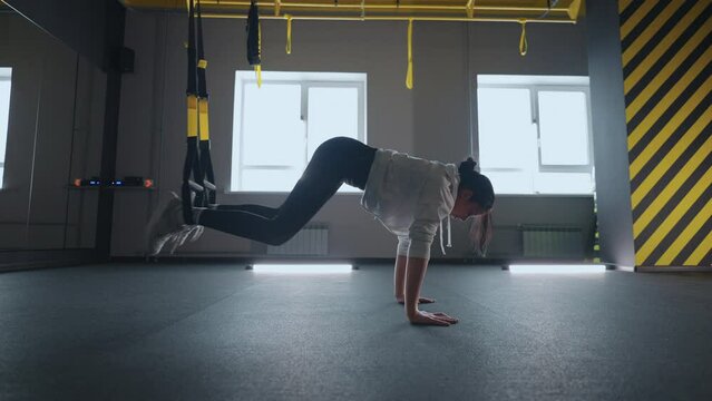 Crossfit fitness TRX training exercises at gym woman push-up workout. Attractive woman doing exercise for hands in gym. core abs crossfit oblique training with fitness straps in the gym's studio. TRX