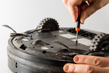 the serviceman unscrews the bolts on the lid of the faulty robot vacuum cleaner with a screwdriver.