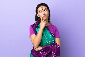 Indian woman isolated on purple background having doubts while looking up