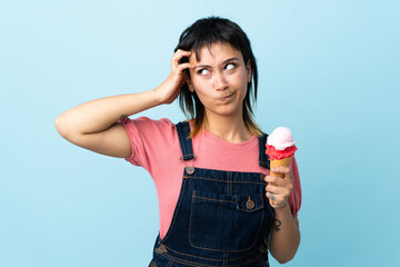 Young Uruguayan girl holding a cornet ice cream over isolated blue background having doubts and...
