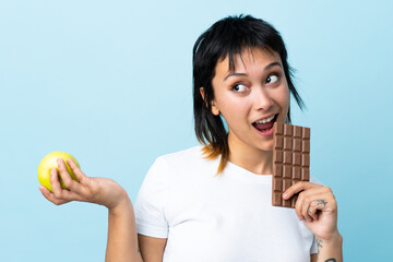 Young Uruguayan woman over isolated blue background taking a chocolate tablet in one hand and an...