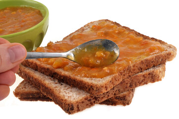 Tranches de pain de mie avec de la confiture de clémantines et une cuillère et un ramequin de confiture sur fond blanc