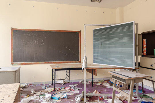 Abandoned and run-down empty classroom, view two chalkboards among a lot of clutter