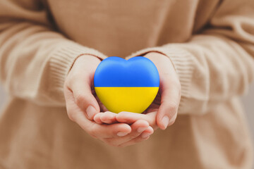 The concept of ending the war in Ukraine. Women's Hands holding the ukraine flag painted heart. Family, patriotism, unity, support.