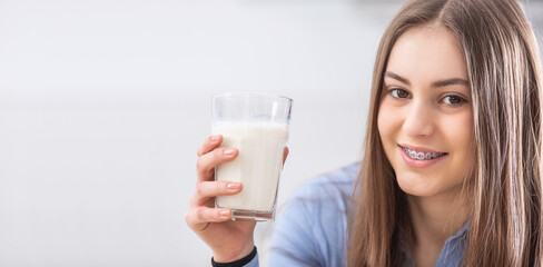 Smiling pretty teenage girl with dental braces holds a glass of fresh milk