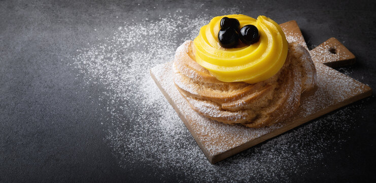 Italian dessert, Zeppola di San Giuseppe, baked cake garnished with custard and sour cherries in syrup, on gray background, space for text, close-up..