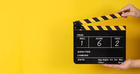 Hands are holding black and yellow clapper board or movie slate with a number on yellow background..