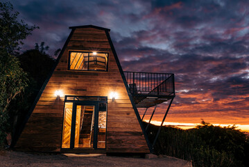 Exterior of a beautifully lit log cabin with a beautiful sunset in the background. 