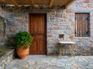 Fototapeta na wymiar A natural wood door and low stonewall fence with trees and potted plants, Pachia Rahi village, Aegina island, Greece
