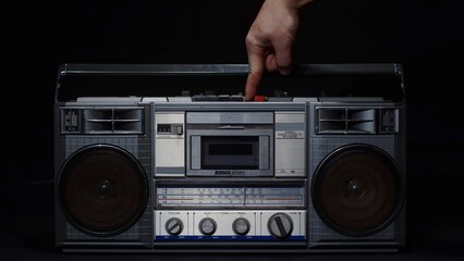 A man's hand with a finger presses the play button on an old vintage gray cassette tape recorder