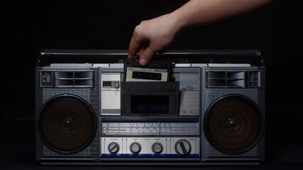 A man's hand inserts a cassette into an old vintage cassette recorder and presses the play button