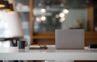 Laptop Computer, notebook, and eyeglasses sitting on a desk in a large open plan office space after...