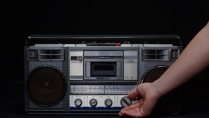 A man's hand turns the frequency adjustment knob of an old fm receiver on a black background