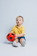 Cheerful little boy 5-6 years old football fan in a yellow T-shirt, supports the team, holds a soccer ball in his hands, isolated on a white background. The concept of sports family recreation