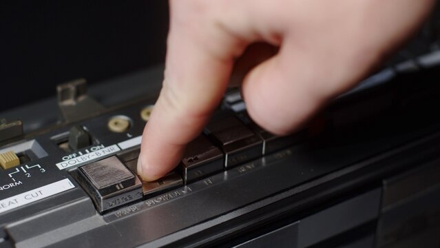 Close-up of a finger that presses the stop button on an old silver shiny cassette recorder