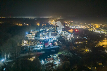 Panorama małego prowincjonalnego miasta w nocnej scenerii. W centrum kadru widać jaskrawo oświetloną fabrykę. Zdjęcie z wysokości wykonane z użyciem drona.