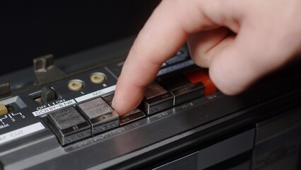 A finger presses the rewind button on a dusty panel on an old tape recorder
