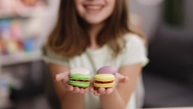 Lovely eticing girl extending to the camera her hands with two delicious macaroon sweeties, smiles her mouths. Focus on the macaroons. Feeling good, delicious.