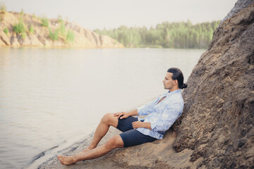 Fototapeta na wymiar A man with dark long hair sits on a sandbank