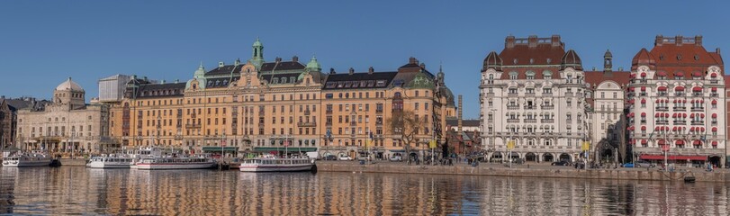 Fototapeta na wymiar Panorama view at the water front pier with apartment and hotel houses, commuting boats in in the calm water bay Ladugårdsviken a sunny winter day in Stockholm