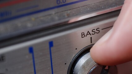 The hand turns the bass volume control on the music device. Bass to the maximum - macro