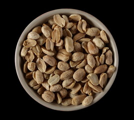 Pile salted and marinated peanuts in bowl isolated on black, top view