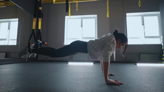 Crossfit fitness TRX training exercises at gym woman push-up workout. Attractive woman doing exercise for hands in gym. core abs crossfit oblique training with fitness straps in the gym's studio. TRX