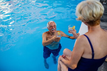 Senior couple on edge of swimming pool drinking lemonade and enjoying summertime together