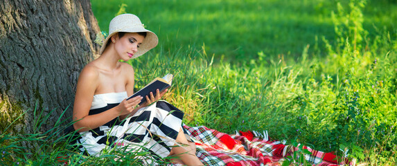 Young beautiful elegant woman reading book on the sunny summer meadow