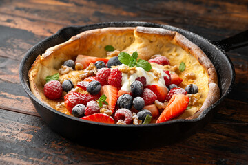 Dutch baby pancake with berries and icing sugar in a iron cast pan. Morning breakfast