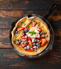 Dutch baby pancake with berries and icing sugar in a iron cast pan. Morning breakfast