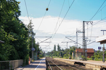 Perspective view of train tracks and platform at Elmshorn train station, Germany in summer with clouds in sunny blue sky background. No people.