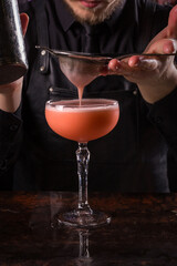 Bartender dressed in black apron and shirt make alcohol cocktail drink on black background