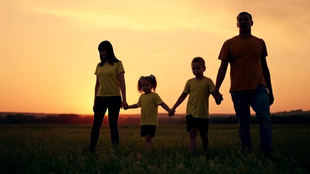 Happy family. Children with parents in park on grass. Family fun at sunset. Silhouette people are walk in park.Summer walk in park. Child holds hand of parents.Happy family concept.Free family in park
