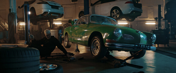 50s Adult Caucasian male mechanic repairing a vintage old car in a workshop, working under car bottom