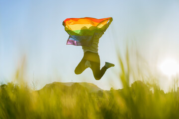 Unrecognizable man jumping with LGBT flag in a field at sunset - obrazy, fototapety, plakaty