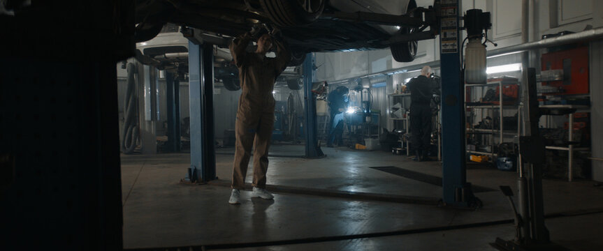 Caucasian female mechanic repairing a car in a workshop, working under car bottom