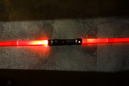 Ein rotes Spielzeug Laserschwert liegt auf dem Boden in einem sanften Lichteinfall . Spooky Star Wars Toy lightsaber in Jedi action . Rotes Lichtschwert . Grauer Metalluntergrund im Raumschiff . 