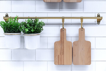 Wooden cutting boards and pots of flowers on the hooks of a kitchen metal rail.