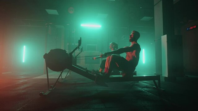 Muscular man and sporty woman workout on training simulator in crossfit gym. Muscular sporty man and women workout on training simulator in gym. Sportswomen exercising on rowing machines
