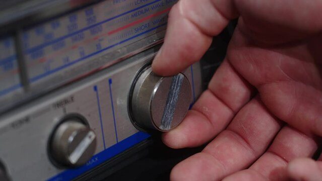 A hand turns the frequency knob on an old gray tape recorder - close-up