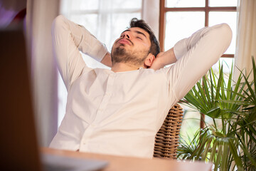 portrait d'un jeune homme qui se détend et s'étire devant son ordinateur. Il se repose dans son...